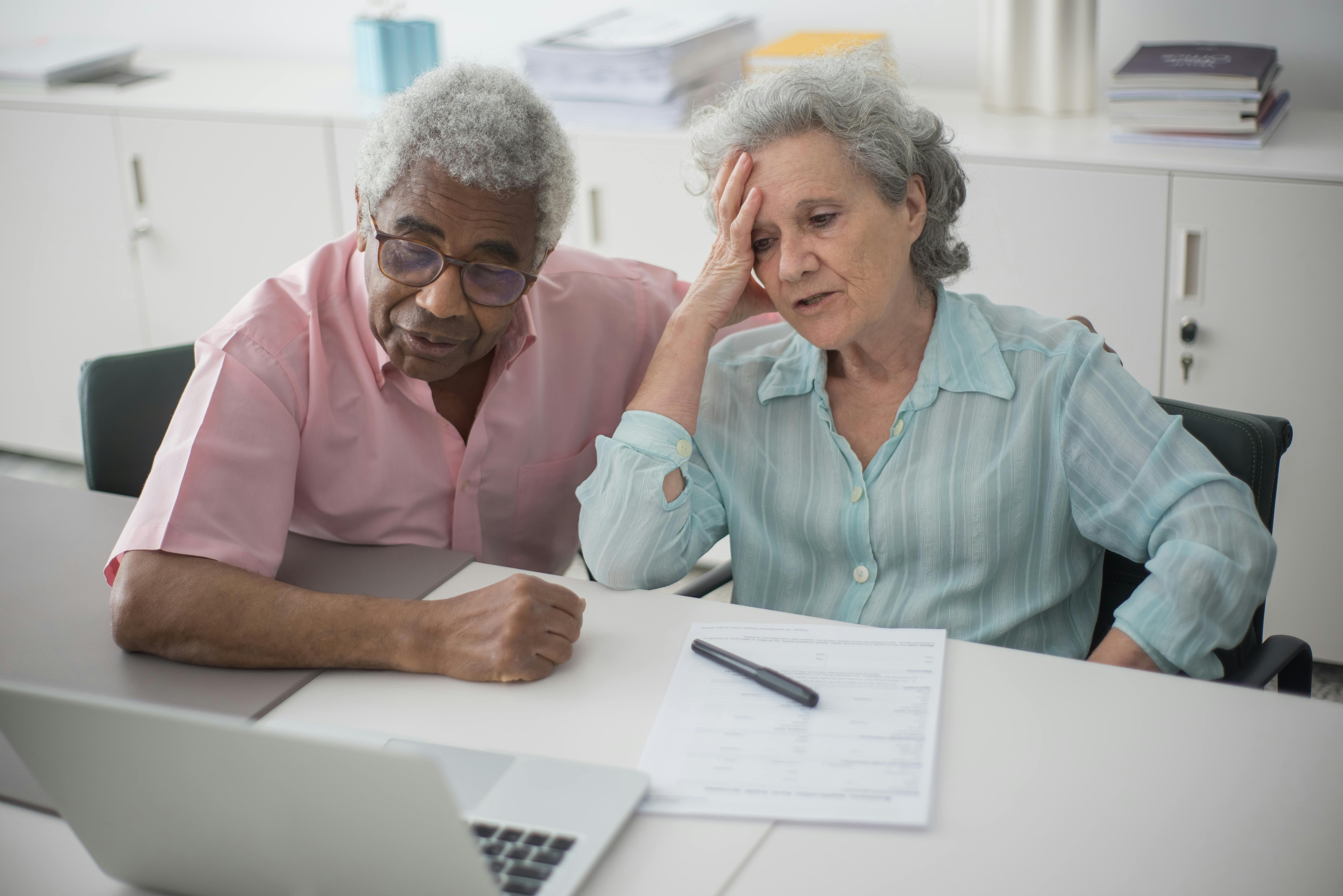 Elderly couple reviewing financial documents and bills on a laptop while looking stressed about solar panel or loan costs.