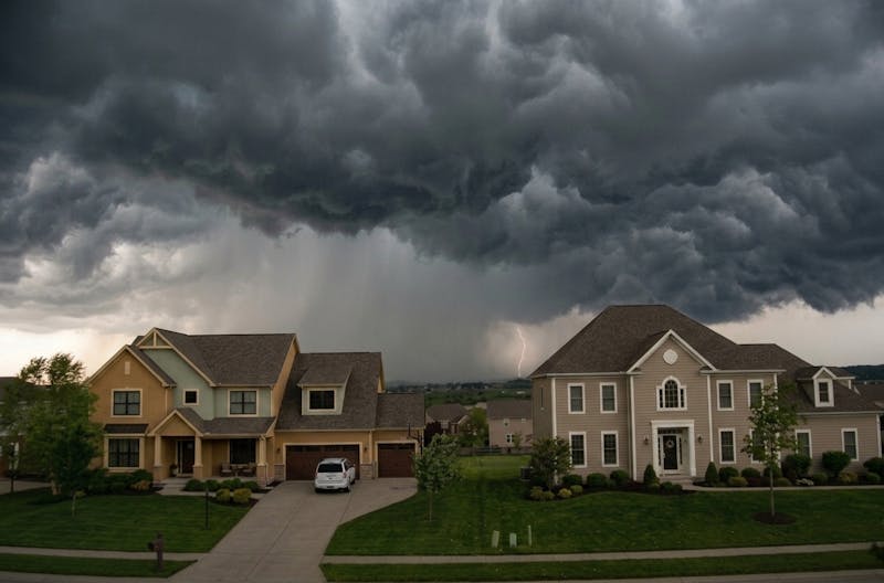 Dark storm clouds and lightning approaching a residential neighborhood as severe weather threatens homes.
