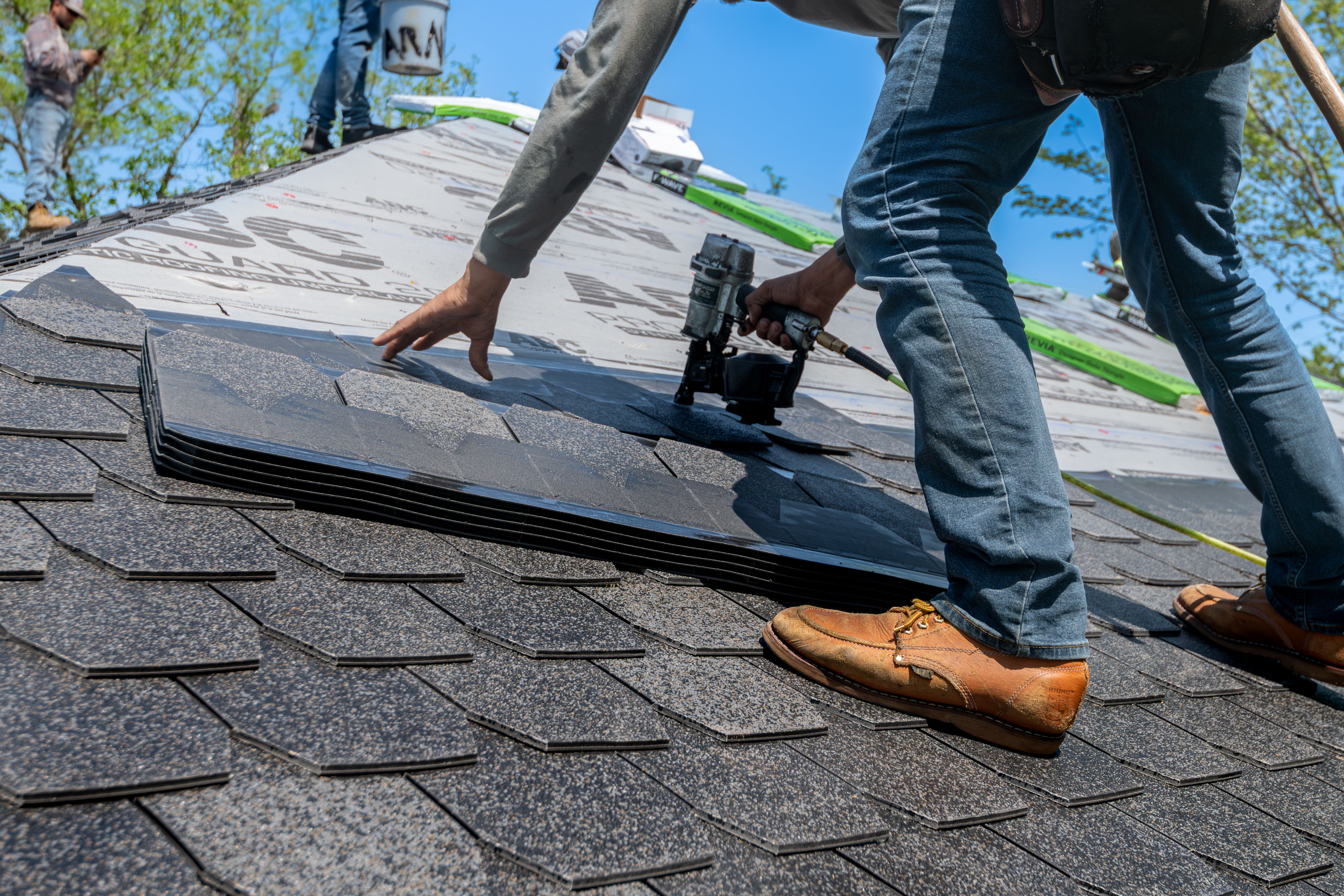 Roofers installing shingles on a residential roof during a roof repair or replacement project.