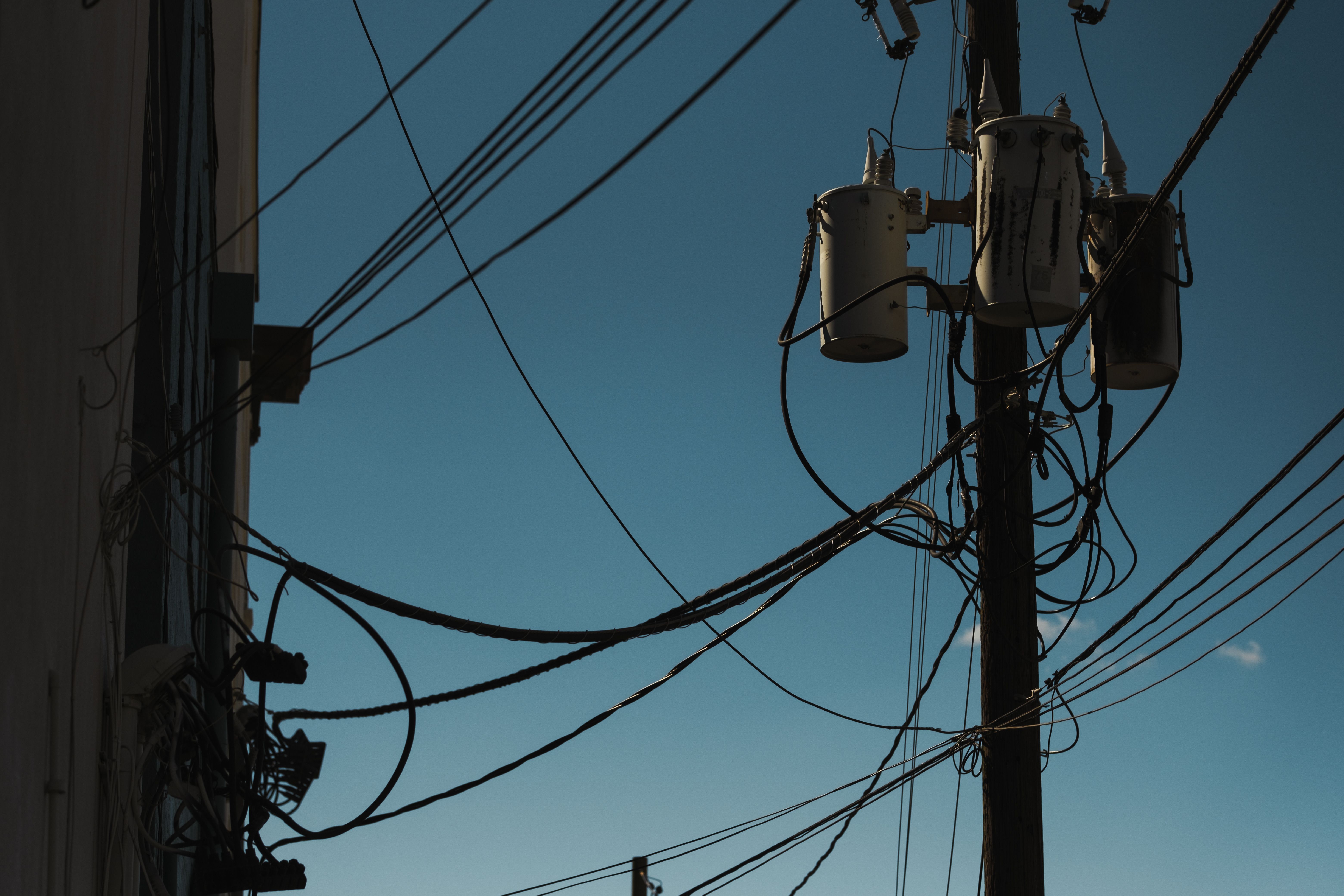 Damaged utility power lines and electrical transformer after a severe storm with clear blue sky overhead.