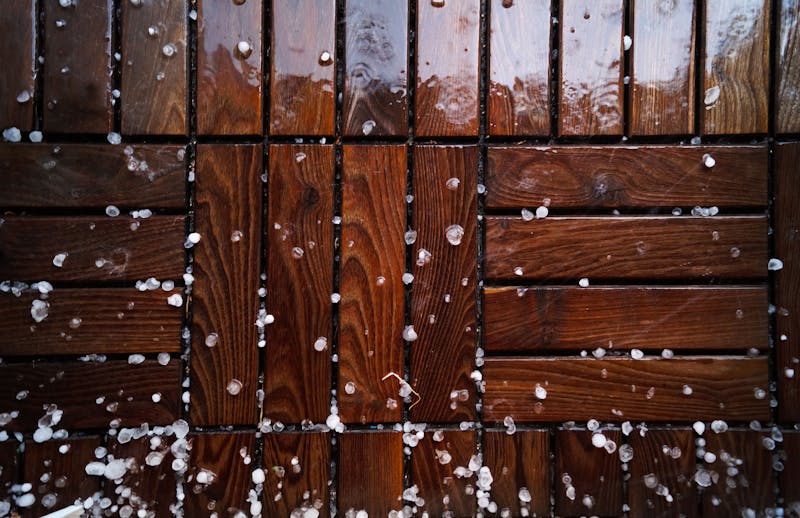 Hail falling and collecting on an outdoor wooden deck during a severe storm.