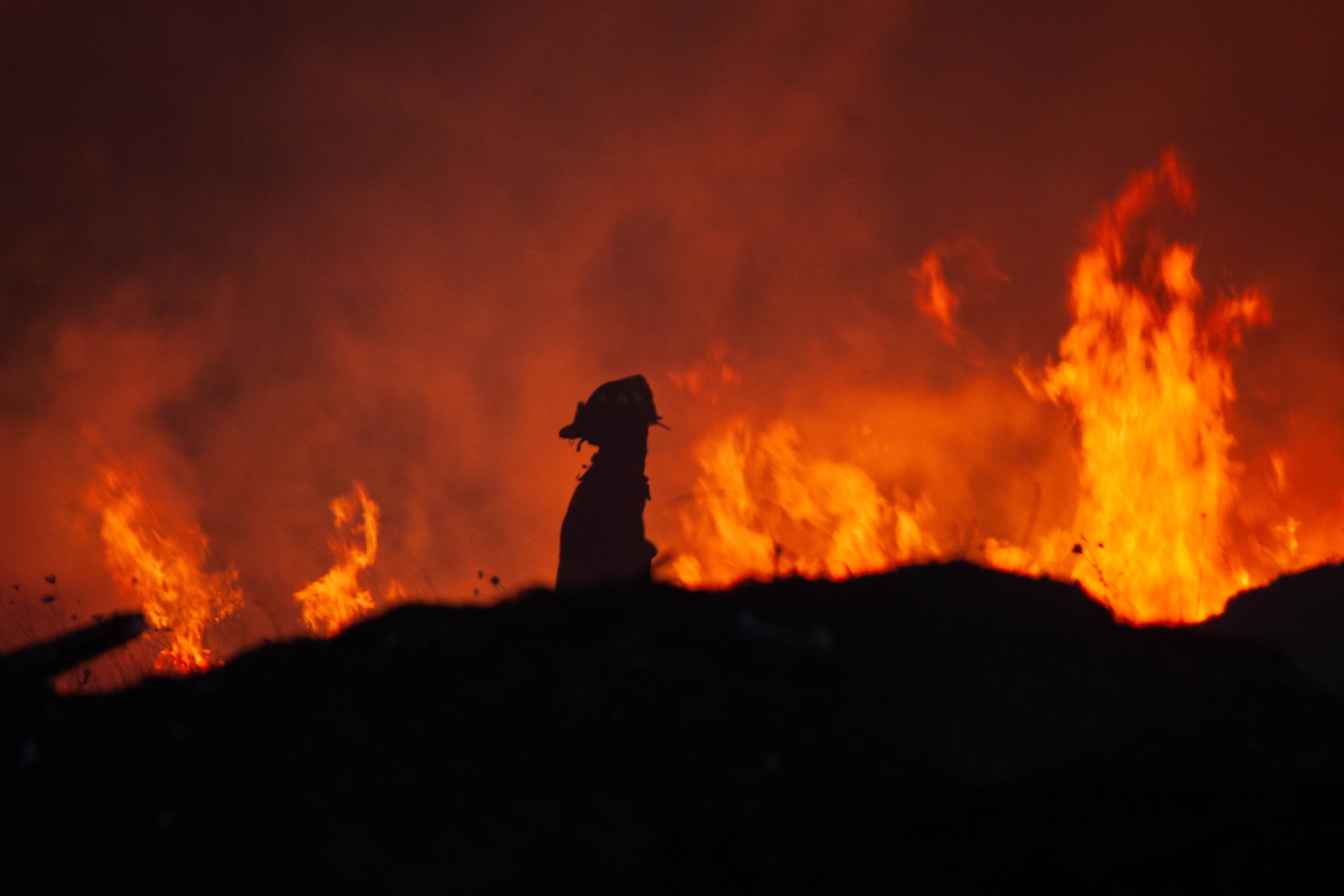 Firefighter standing near flames during a large wildfire