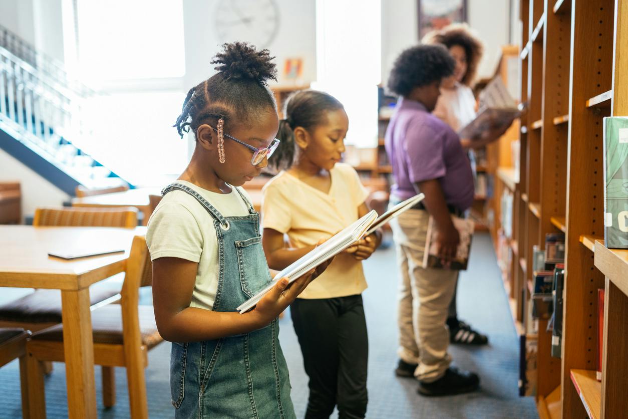 school children with teacher in library, having a reading class
