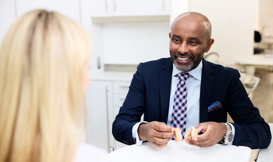 dr sinada with fake teeth in his hands speaking to patient