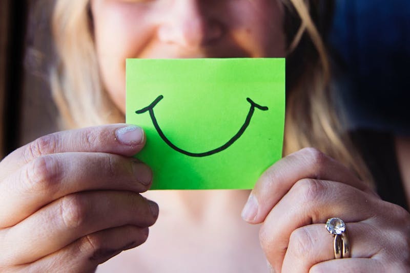 person holding up a green piece of paper with a smile drawn on it