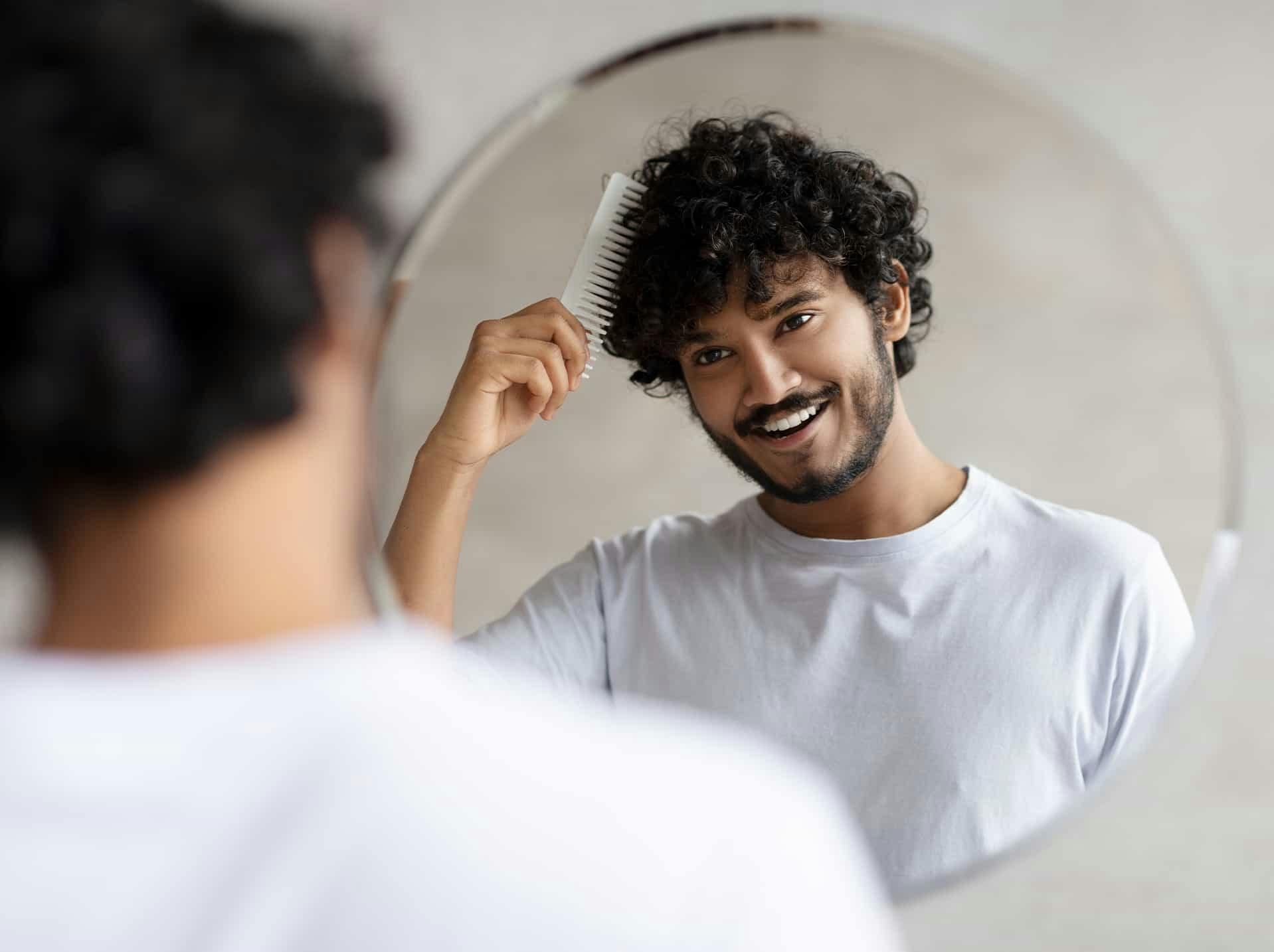 man smiling while combing hair in the mirror