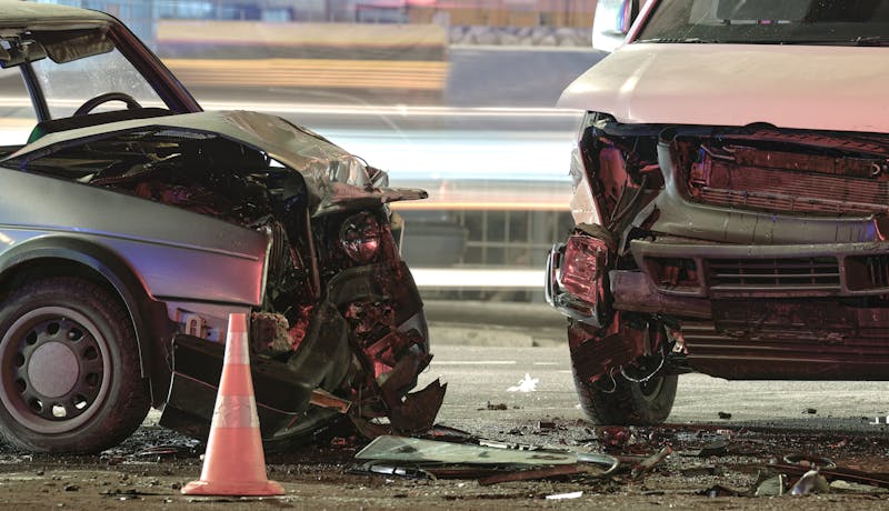 Two heavily damaged vehicles at the scene of a car crash with a traffic cone and debris on the road.