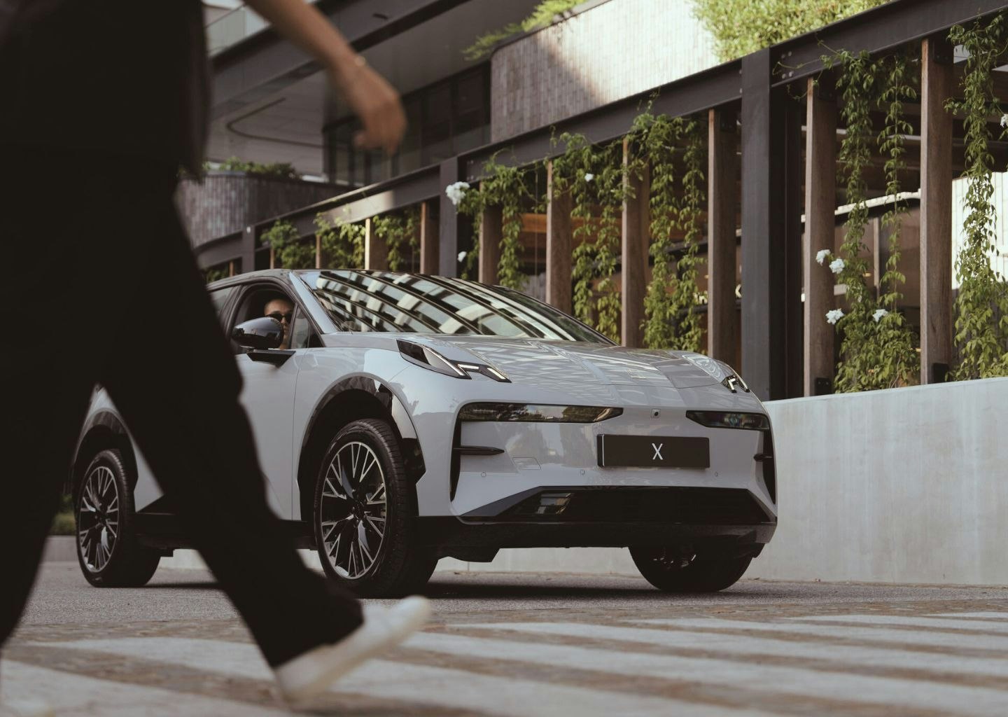 Crystal white ZEEKR X stopping at a cross walk for a pedestrian.