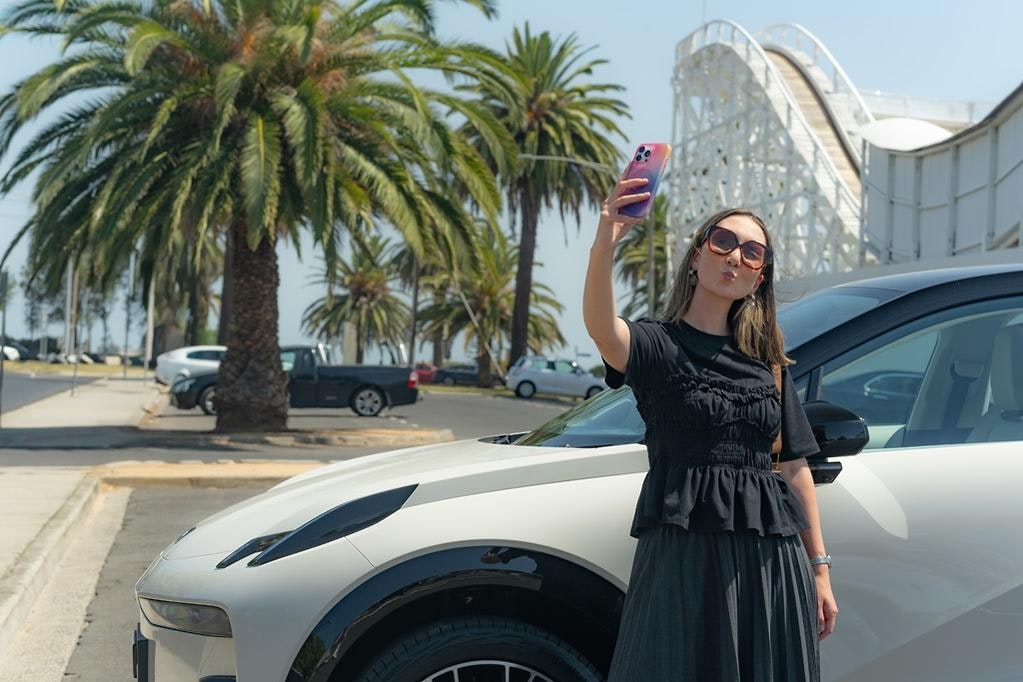 Andrea Hobbs taking a photo in front of the ZEEKR X in Palace Beige at Luna Park in Melbourne.