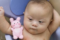 Mixed race Down Syndrome baby laying in plastic bathtub
