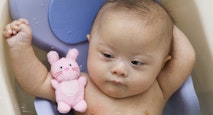 Mixed race Down Syndrome baby laying in plastic bathtub