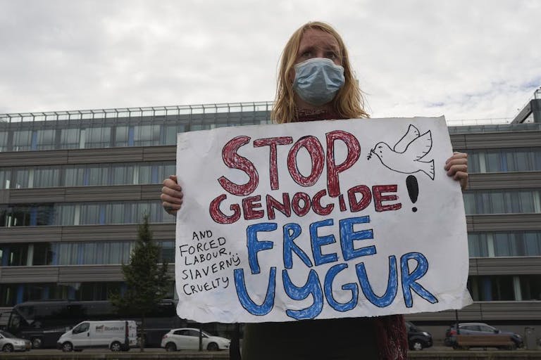 A woman holds a sign stating stop genocide. Organ harvesting, free uyghur. Uyghur, Uighur, Muslims, China, forced genocide.
