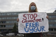 A woman holds a sign stating stop genocide. Organ harvesting, free uyghur. Uyghur, Uighur, Muslims, China, forced genocide.