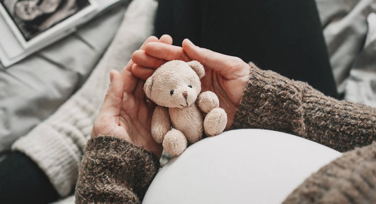 Woman pregnant belly with little teddy toy bear. Concept image with symbol of many meanings for expectant mother during pregnancy and her unborn baby.