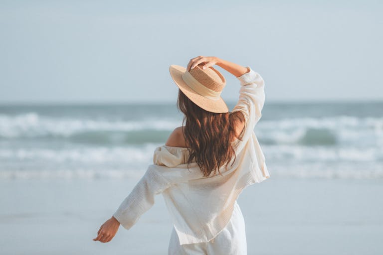 Summer beach vacation concept, Young woman with hat relaxing with her arms raised to her head enjoying looking view of beach ocean on hot summer day, copy space.