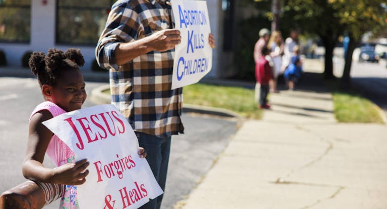 A girl holds a sign reading, Jesus Forgives & Heals as