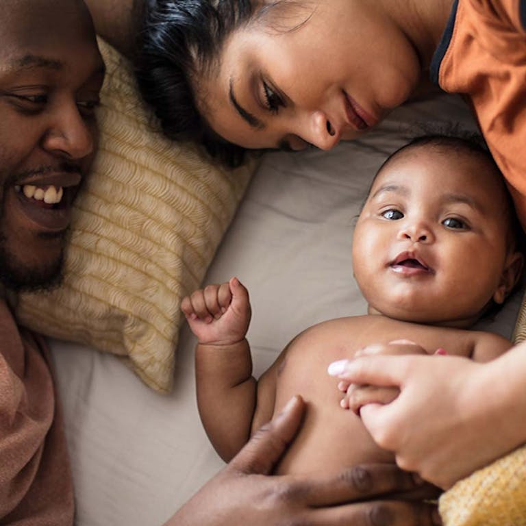 A mother, father, and baby laying down together smiling