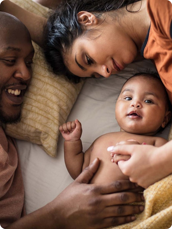 A mother, father, and baby laying down together smiling