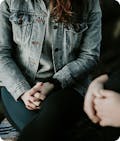 Woman in jean jacket with clasped hands in lap