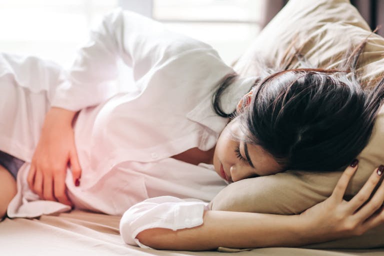 Woman Touching Abdomen In Pain While Sleeping On Bed At Home
