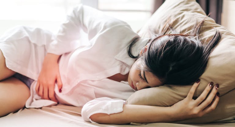 Woman Touching Abdomen In Pain While Sleeping On Bed At Home