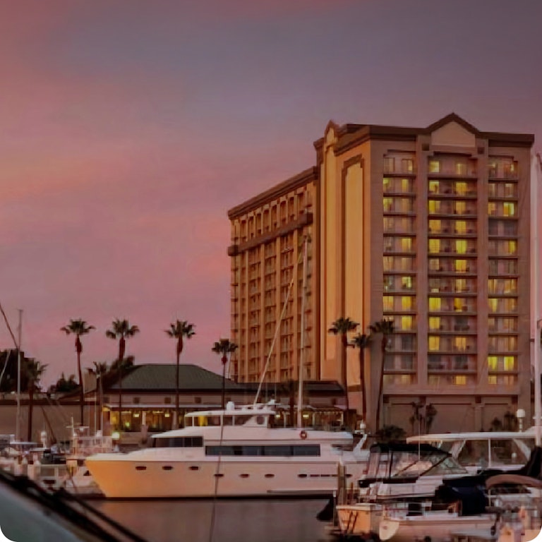 Large hotel and boat against a pink and purple sunset sky