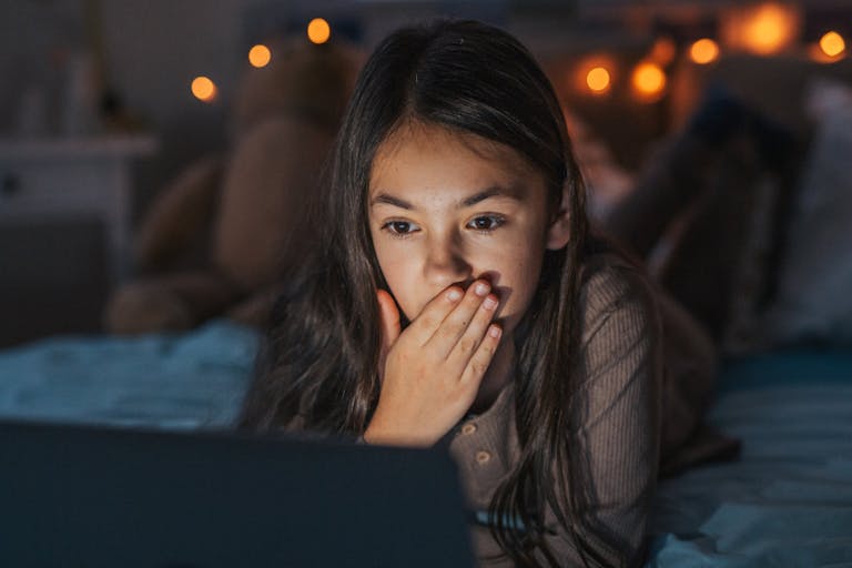 Girl watching inappropriate content on laptop, covering her mouth in shock.