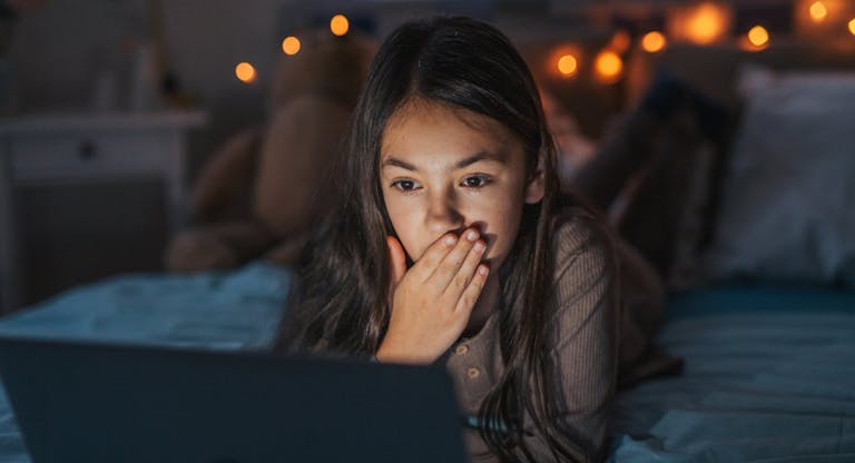 Girl watching inappropriate content on laptop, covering her mouth in shock.