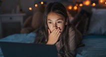 Girl watching inappropriate content on laptop, covering her mouth in shock.