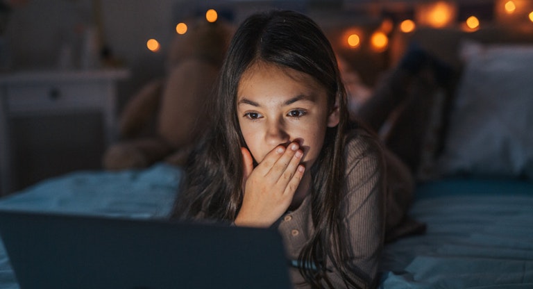 Girl watching inappropriate content on laptop, covering her mouth in shock.