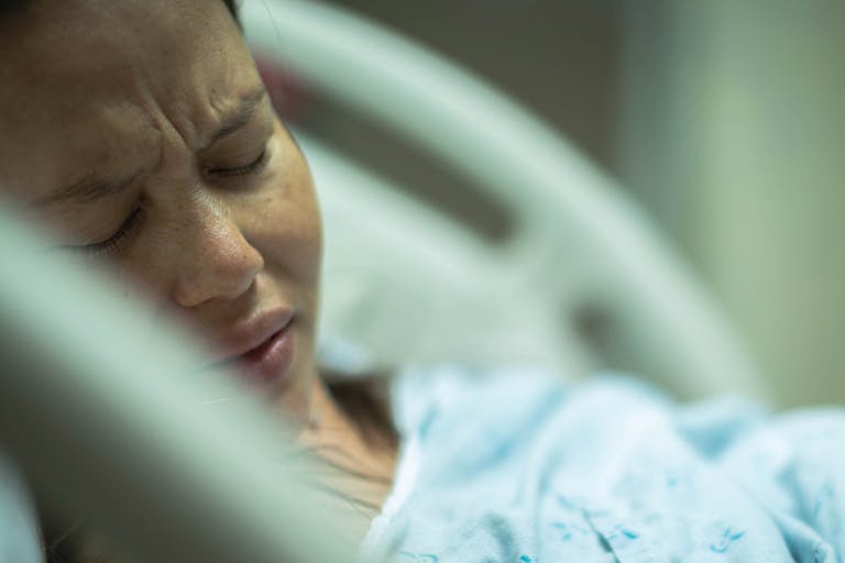 A sick woman patient lying in a hospital bed depressed and in pain.