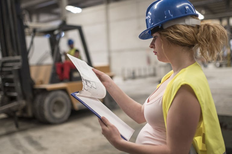 Pregnant worker woman in concrete factory looking note, looking at the work planning plan. Preparing labor