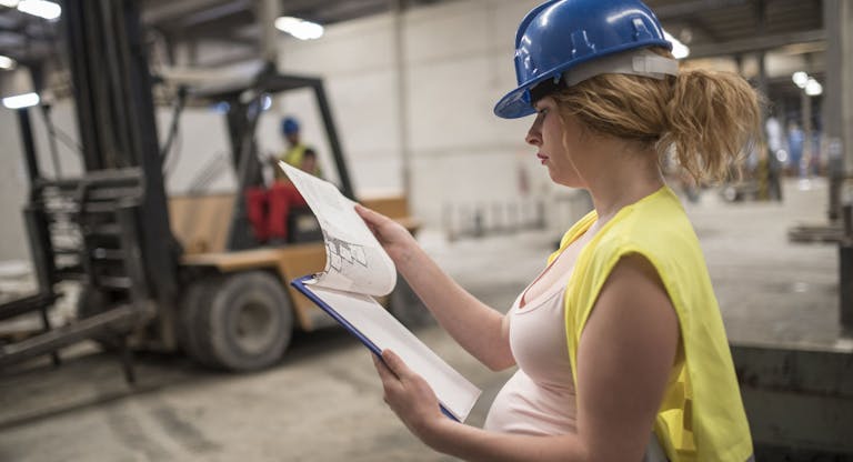 Pregnant worker woman in concrete factory looking note, looking at the work planning plan. Preparing labor