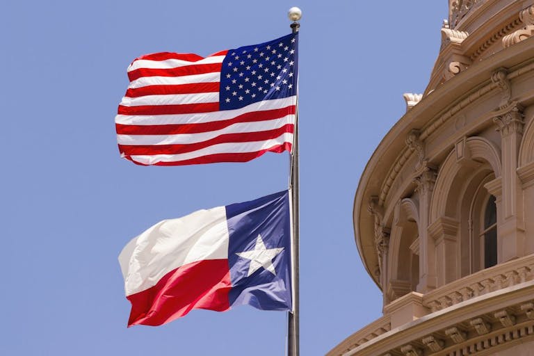 Texas capitol. The Texas flag and US flag fly in front of Texas capitol building.
