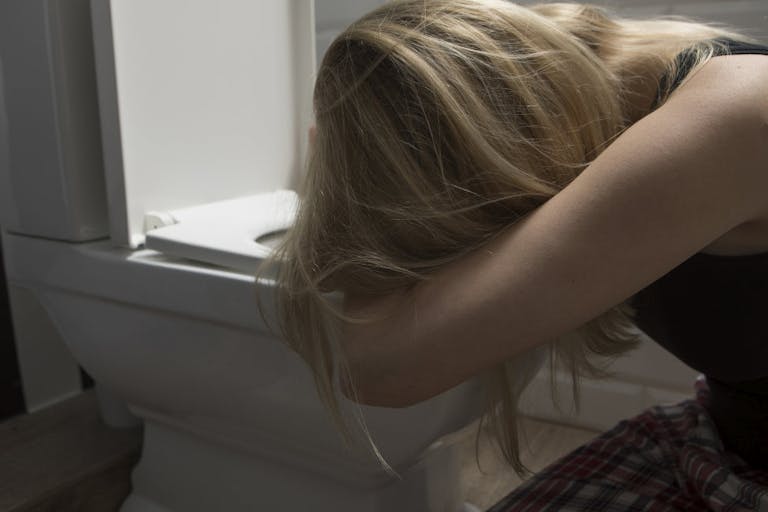 Sad woman kneeling by toilet bowl in bathroom at home