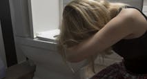 Sad woman kneeling by toilet bowl in bathroom at home