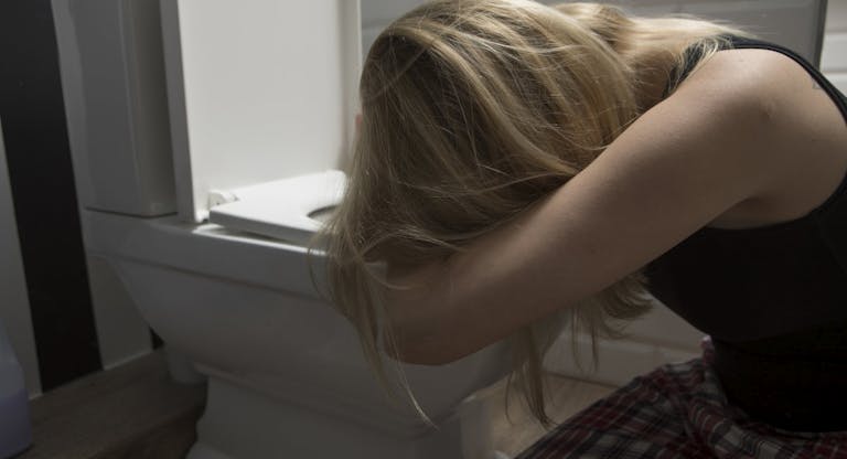 Sad woman kneeling by toilet bowl in bathroom at home
