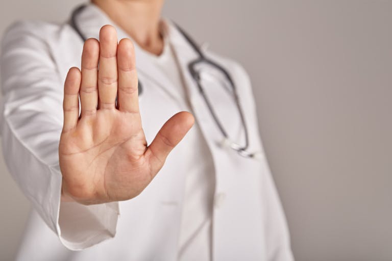 Professional medical doctor in white uniform with a stethoscope around her neck making stop gesture with hand, medicine and healthcare concept