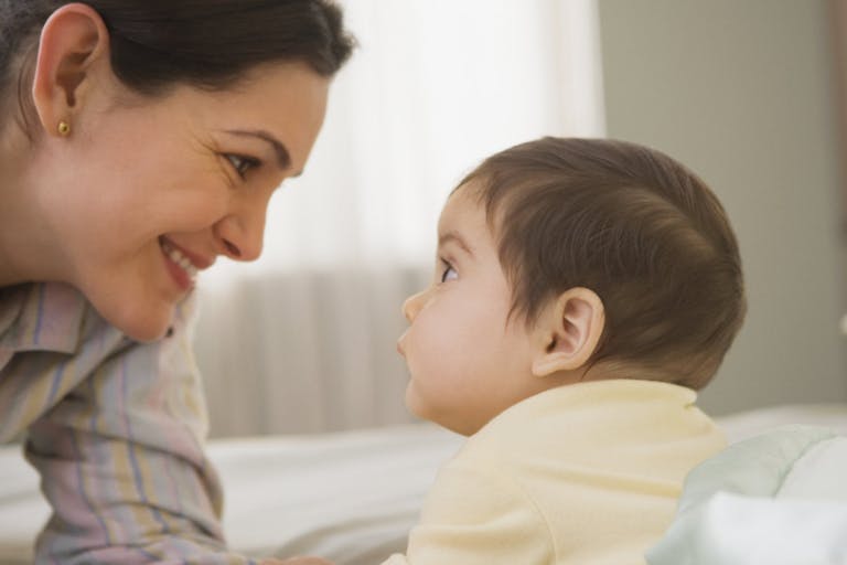 Mother smiling at baby on bed