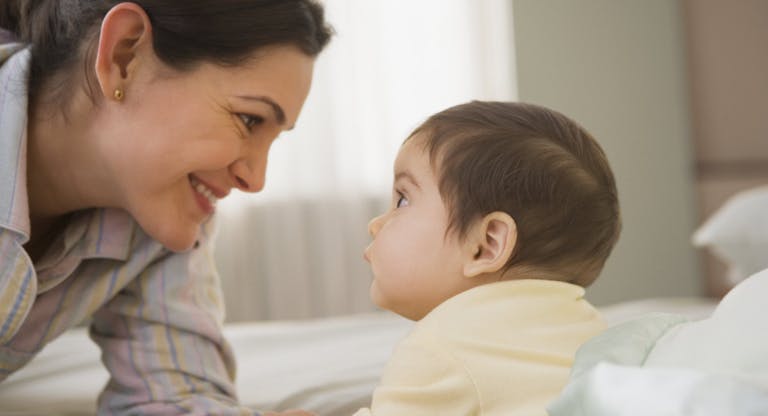 Mother smiling at baby on bed
