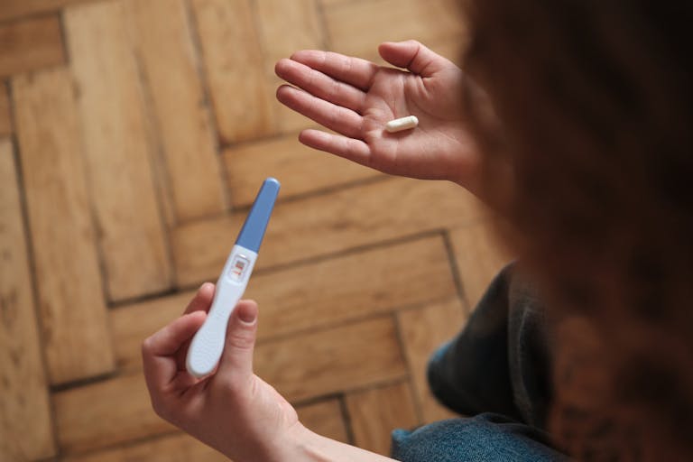 Woman holding pregnancy test and abortion pill while sitting on sofa. At Home Abortions