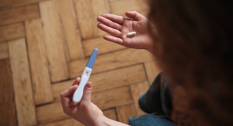 Woman holding pregnancy test and abortion pill while sitting on sofa. At Home Abortions