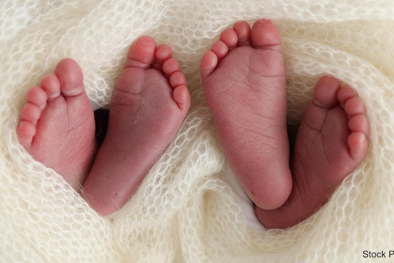 Legs, toes, feet and heels of newborn twins. Wrapped in a knitted white blanket. Studio macro photography of the legs of newborn twins, close-up white backgraund. Two newborns.