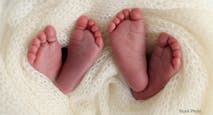 Legs, toes, feet and heels of newborn twins. Wrapped in a knitted white blanket. Studio macro photography of the legs of newborn twins, close-up white backgraund. Two newborns.