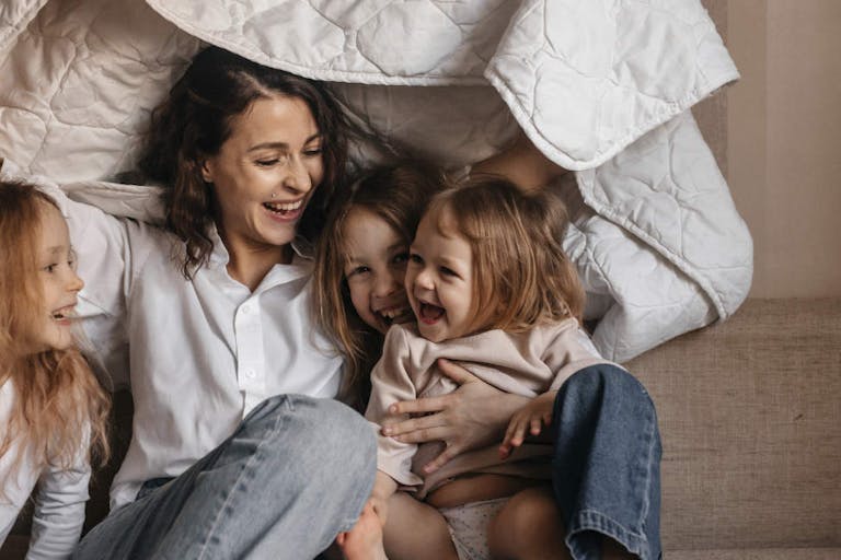 Happy mother with three girls holding blanket on sofa at home