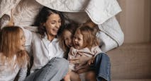 Happy mother with three girls holding blanket on sofa at home