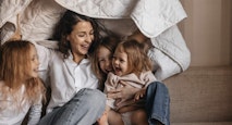 Happy mother with three girls holding blanket on sofa at home