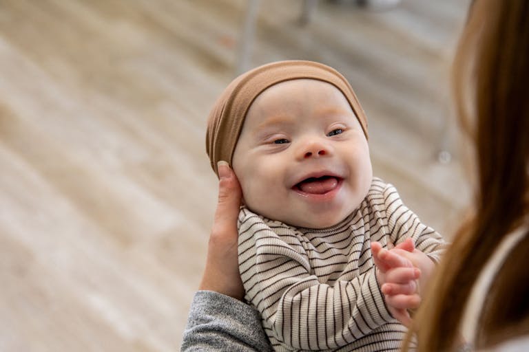 Adorable happy newborn baby with Down Syndrome smiles at his mother