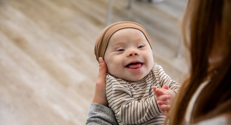 Adorable happy newborn baby with Down Syndrome smiles at his mother