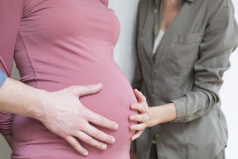 Photo: Getty Images A pregnant woman wearing pink with the hands of a man and woman on her stomach.